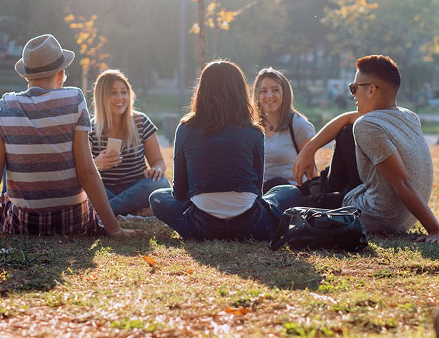 Groupe de jeunes dans un parc urbain, assis en cercle sur l’herbe.